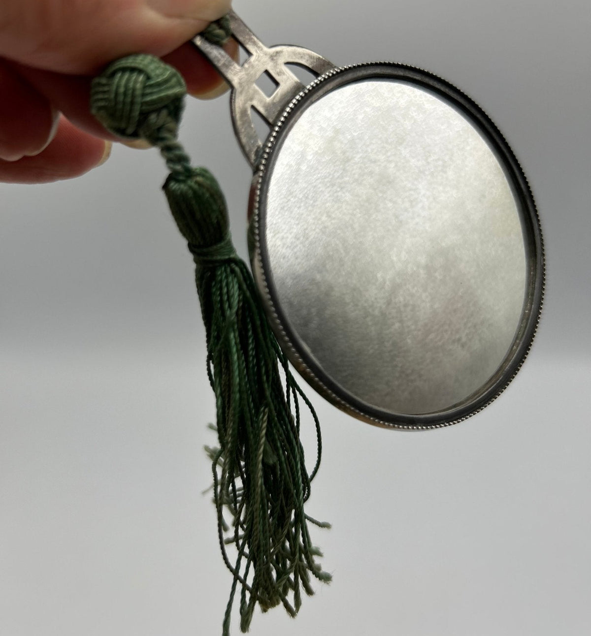 round silver purse mirror held by hand with tassel on grey ground- Splendid Vintage World