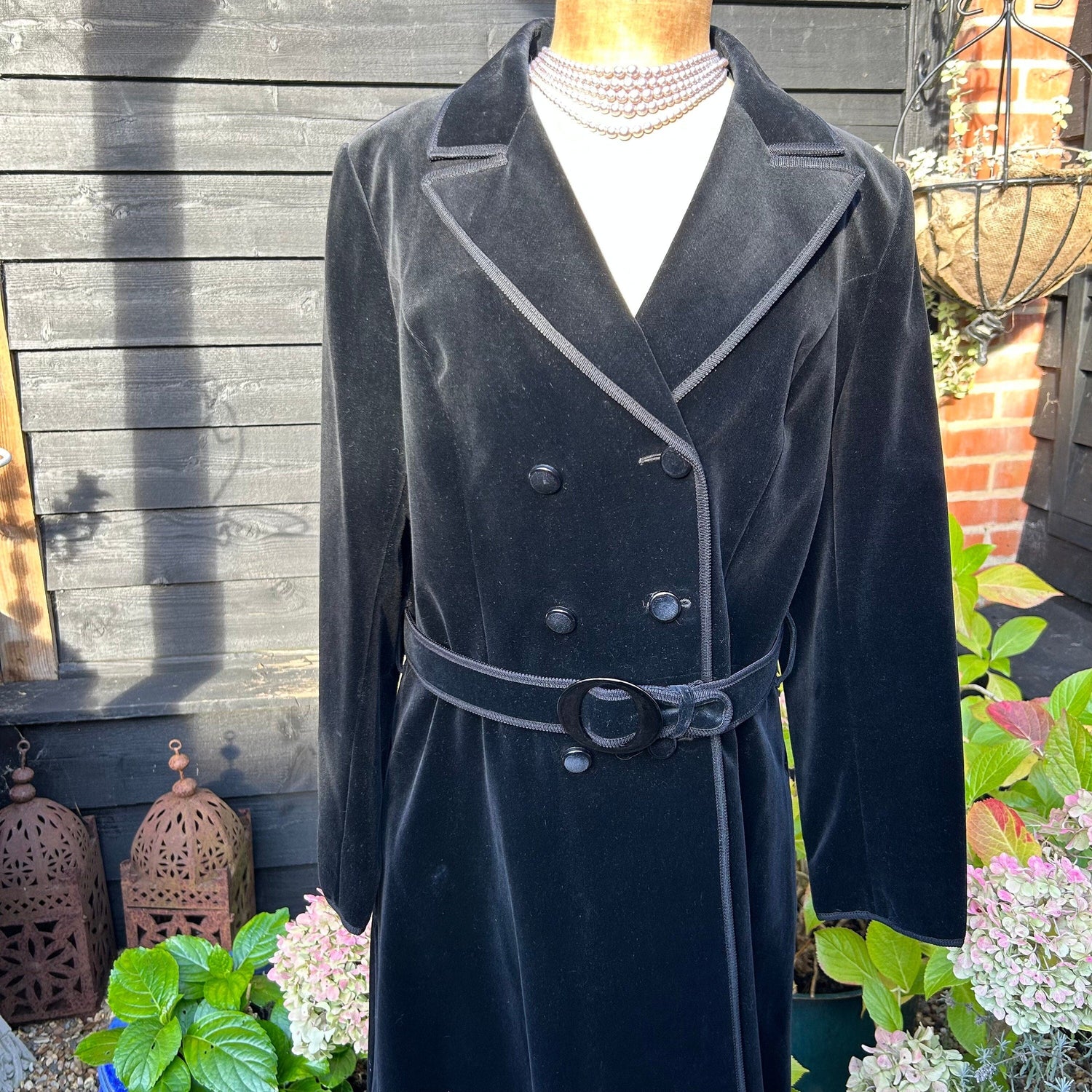 Vintage clothing black double breasted velvet coat on mannequin with plants & black fence behind - Splendid Vintage World