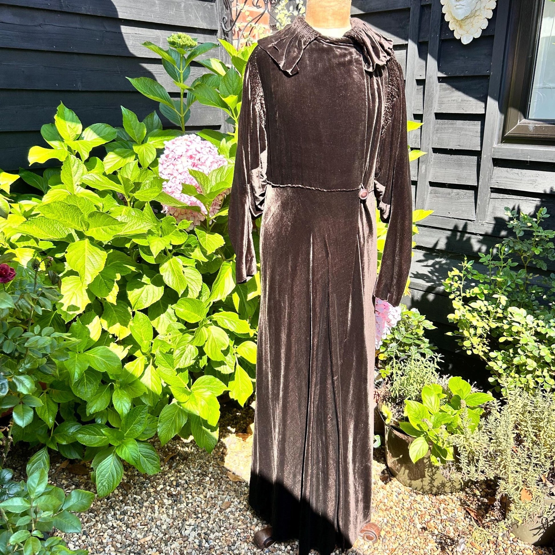 vintage Dark Brown long Velvet Coat on a mannequin against green plants & black fence - Splendid Vintage World