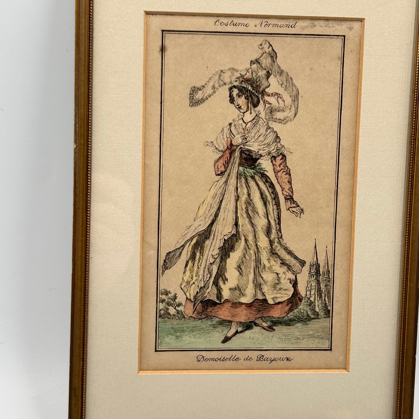 antique framed print of a woman in historical Normandy costume with 2 church spires in background - splendid vintage world