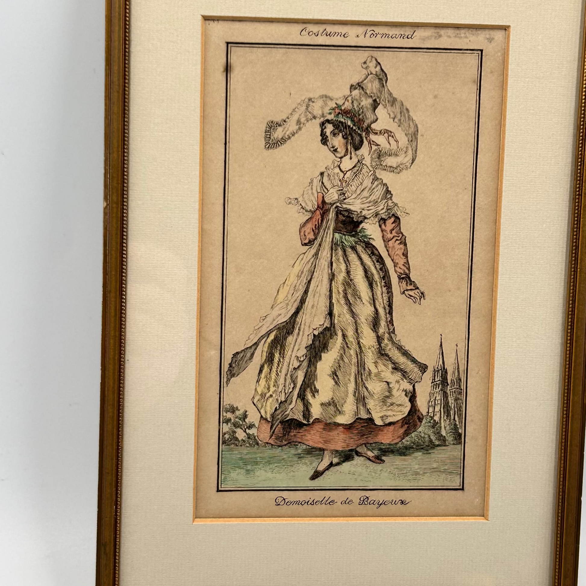 antique framed print of a woman in historical Normandy costume with 2 church spires in background - splendid vintage world