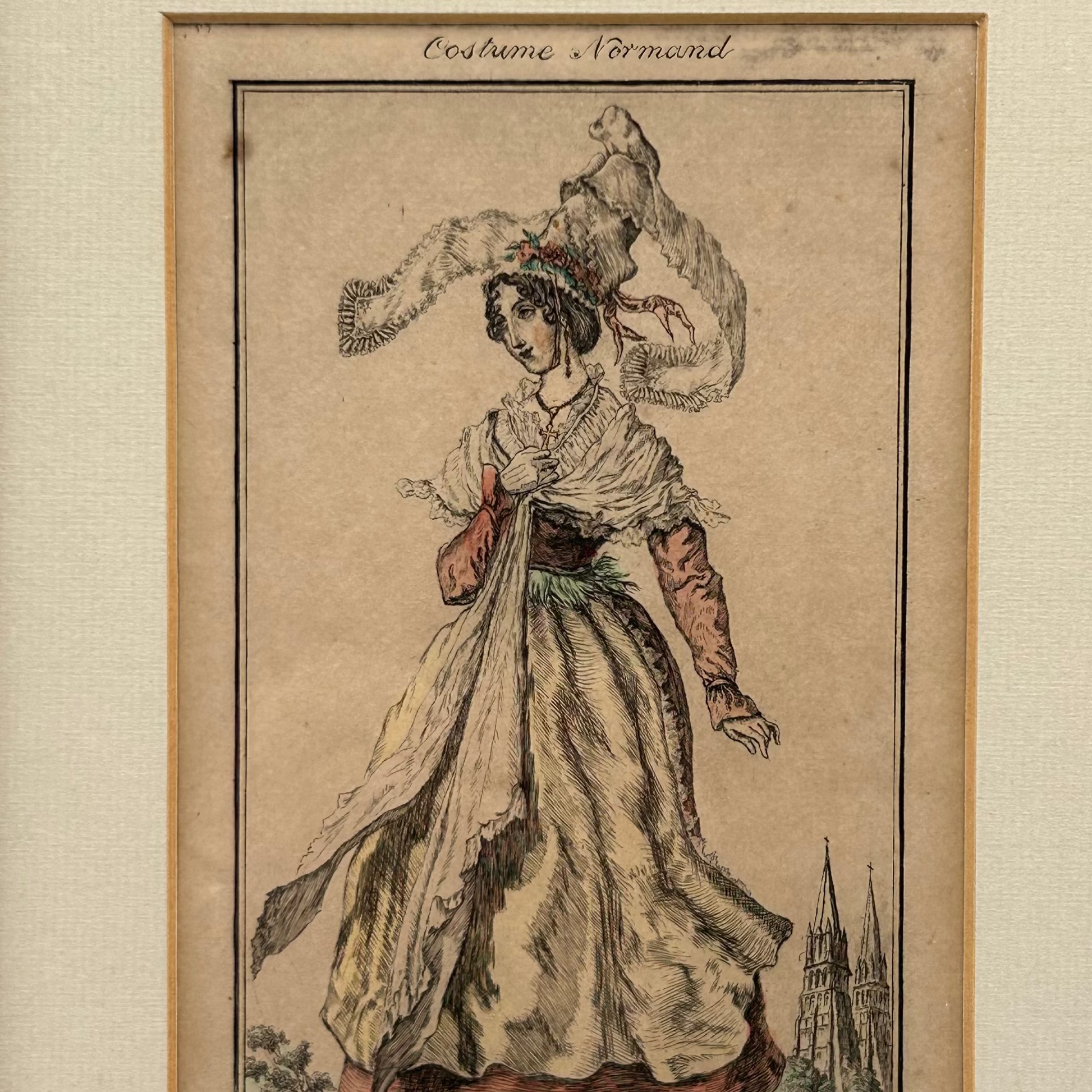 Antique print of a woman in Normand costume in tall hat on a beige paper featuring a church with 2 spires in the distance