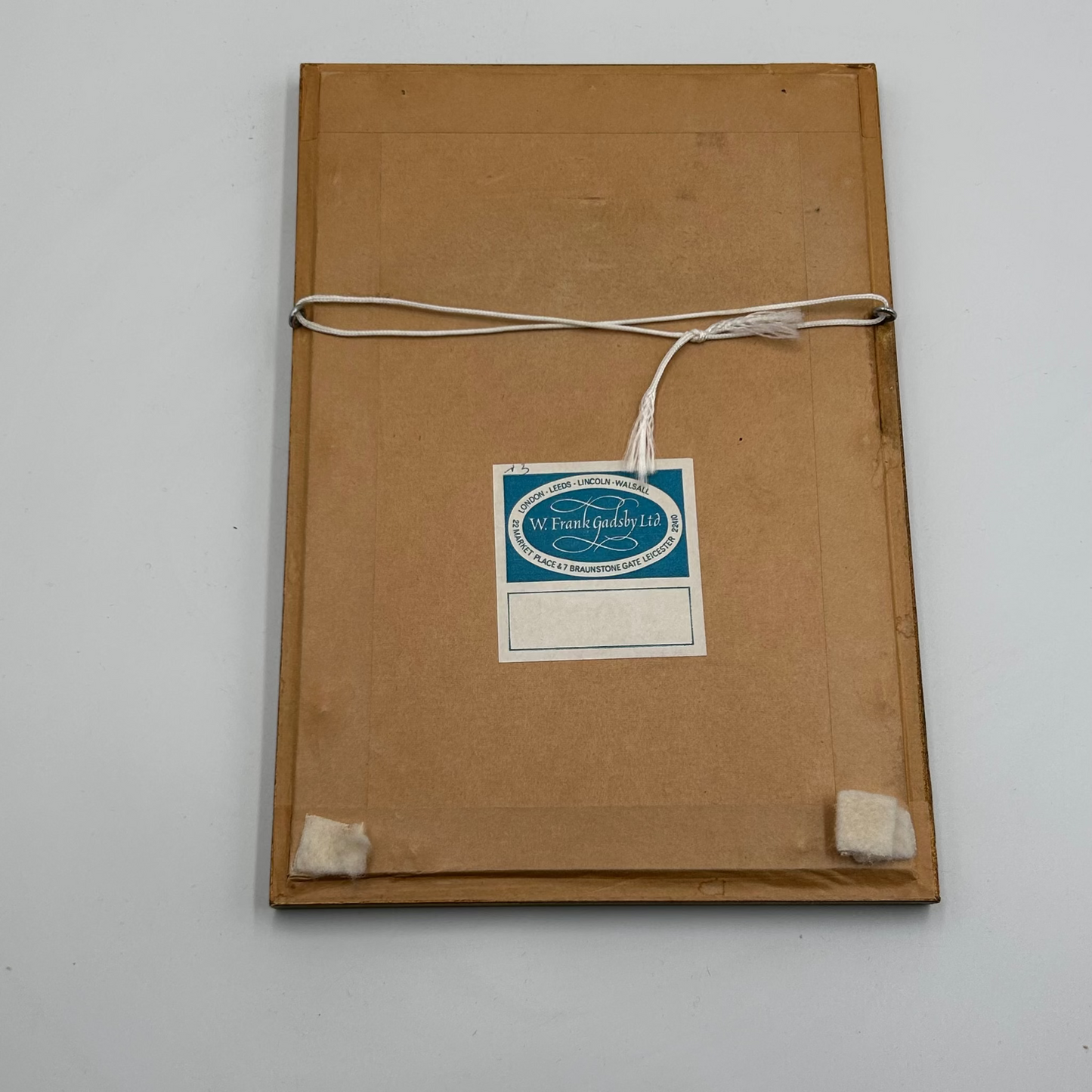Brown paper backing on the reverse of a frame with framers label and white cord on white background - splendid vintage world