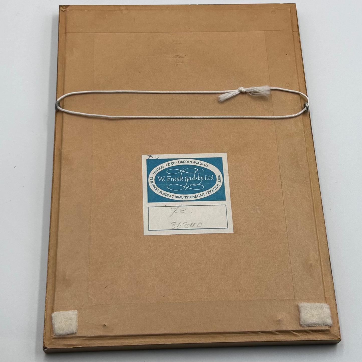 Brown paper back of frame with a framers label & white cord on a white background
