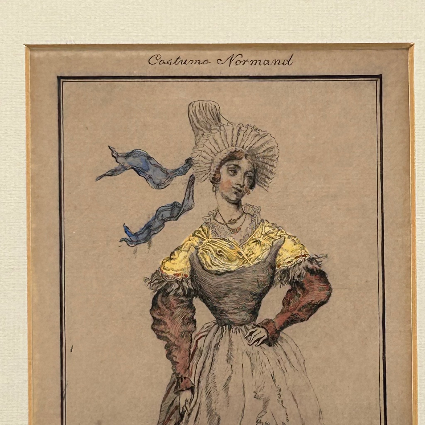 Antique print of woman in Normandy costume with red sleeves, yellow wrap & blue ribbon bonnet framed on light background.