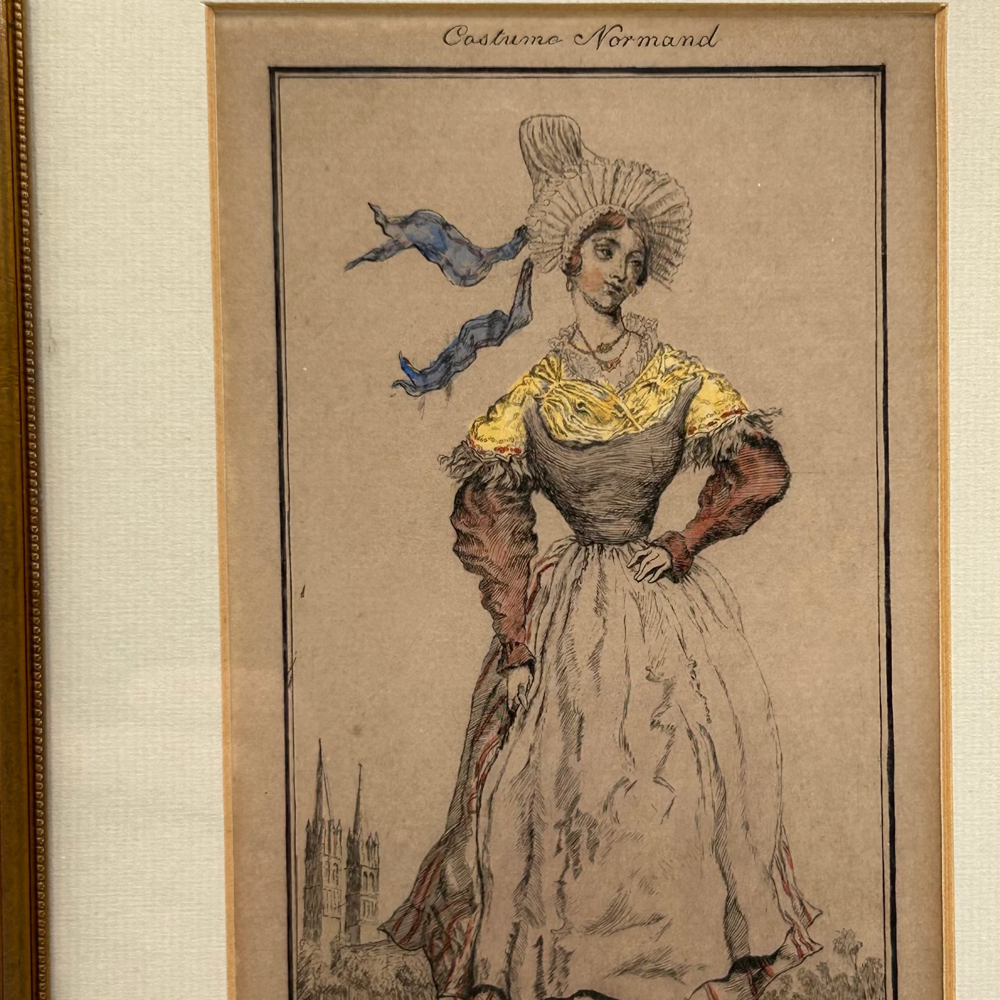 antique print of a woman in Normandy costume with a decorative hat and dress, church spires in background.