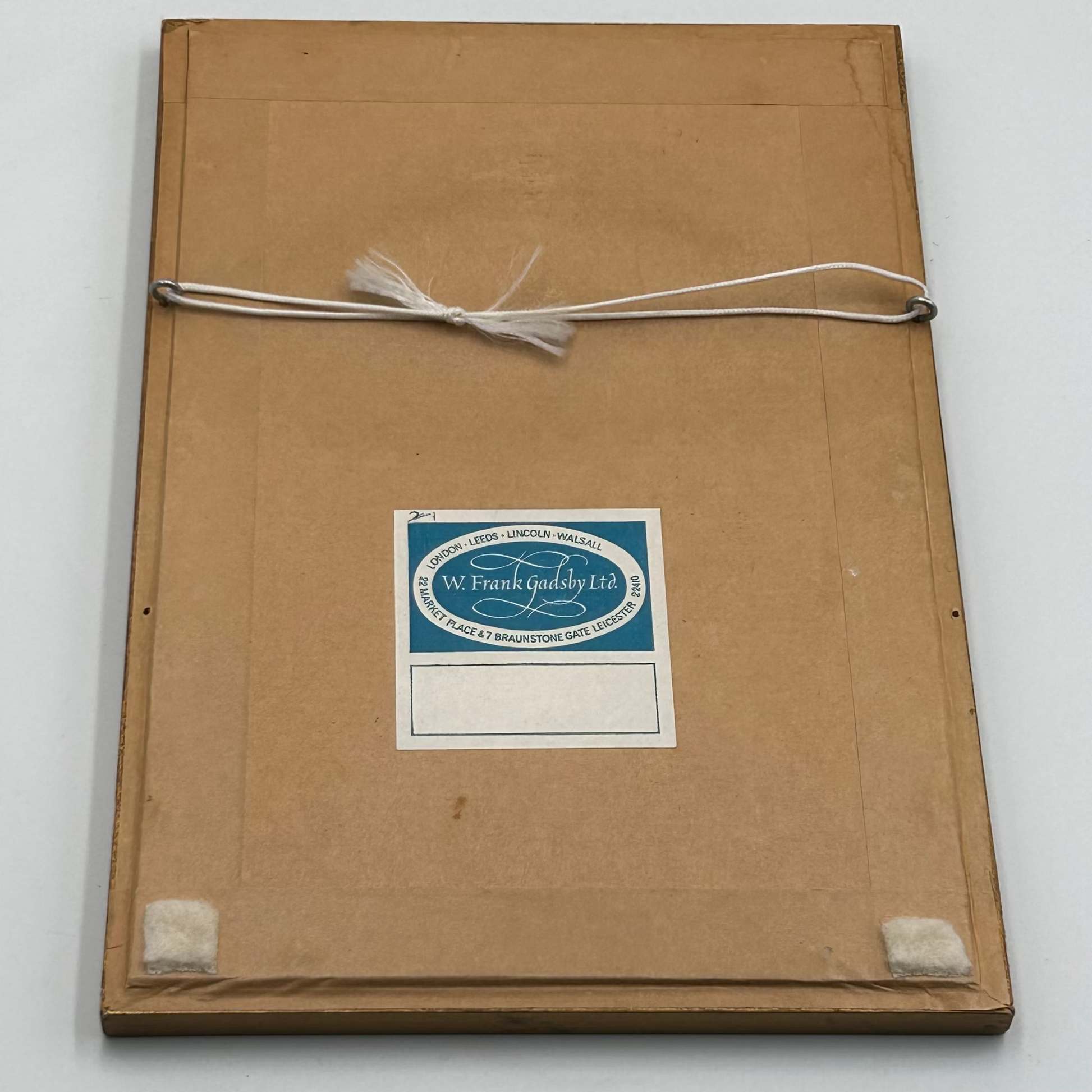 Brown paper backing of a frame with framers label & white cord on a white background