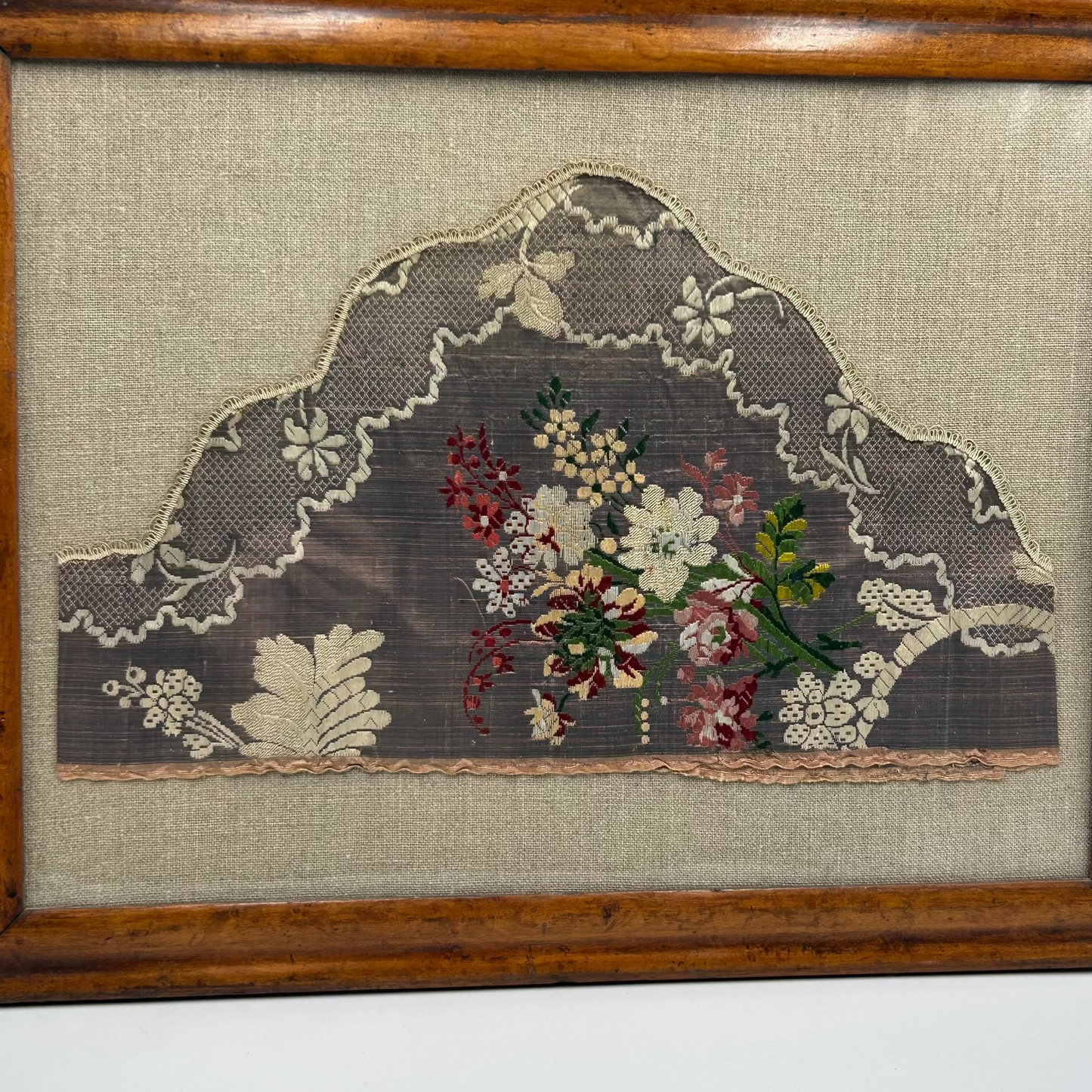 Decorative textile lace panel with floral embroidery in a wooden frame.