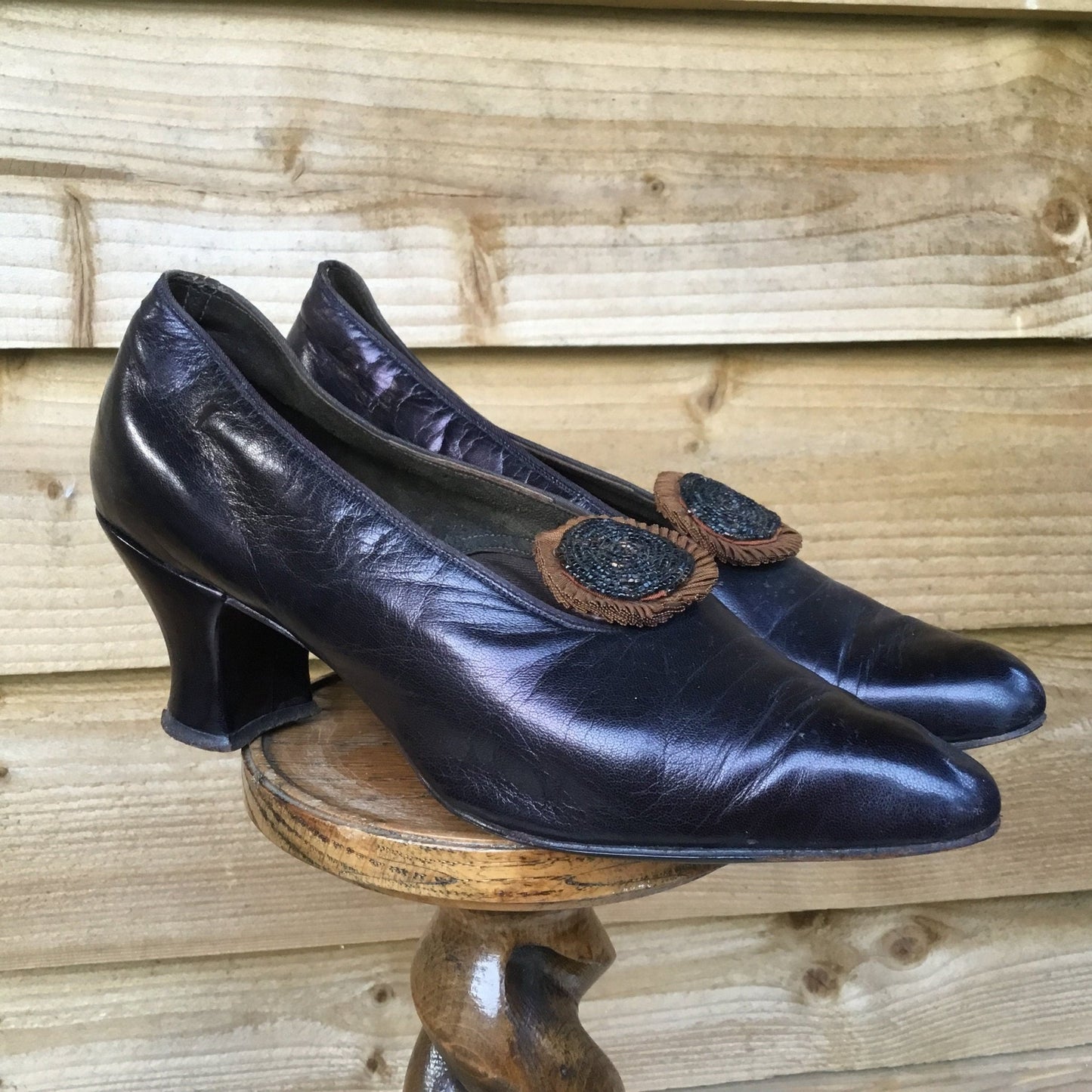 Antique 1910s Leather Shoes with beaded rosettes on wooden stand with fence background - Splendid Vintage World