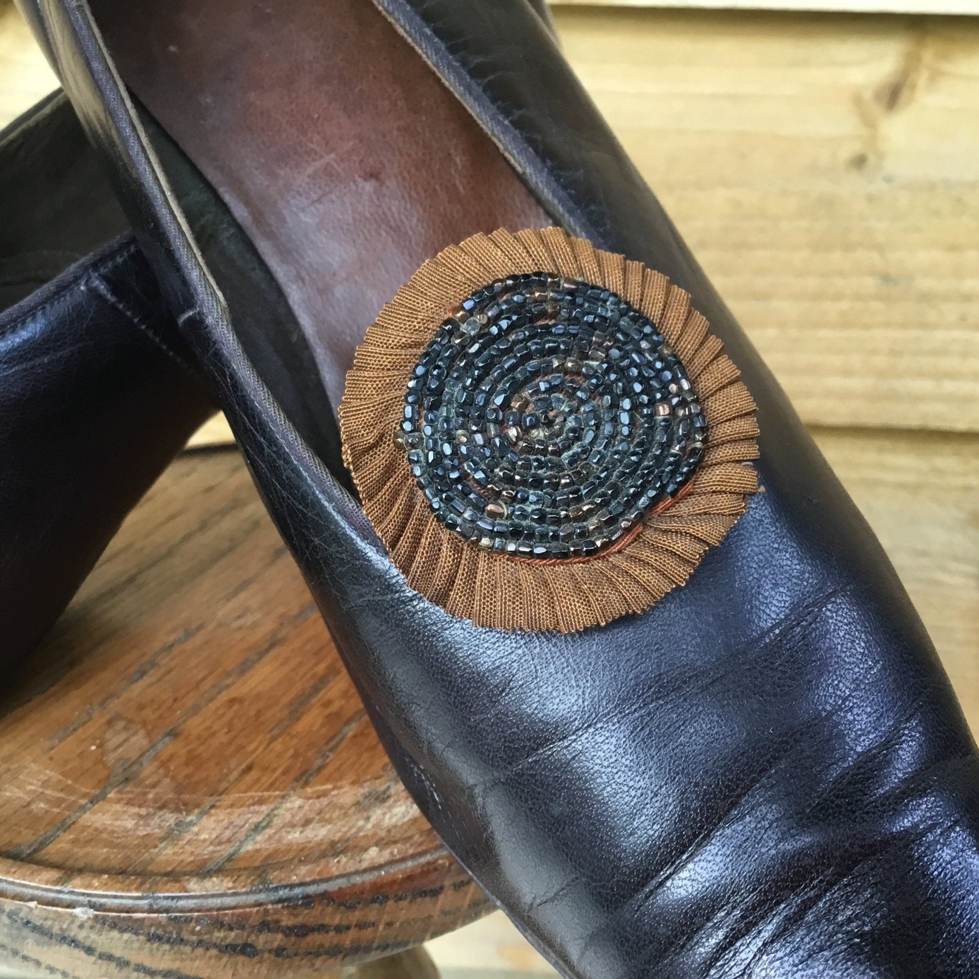close up of Antique Leather Shoe beaded textile rosettes on wooden stand against wooden fence - Splendid Vintage World