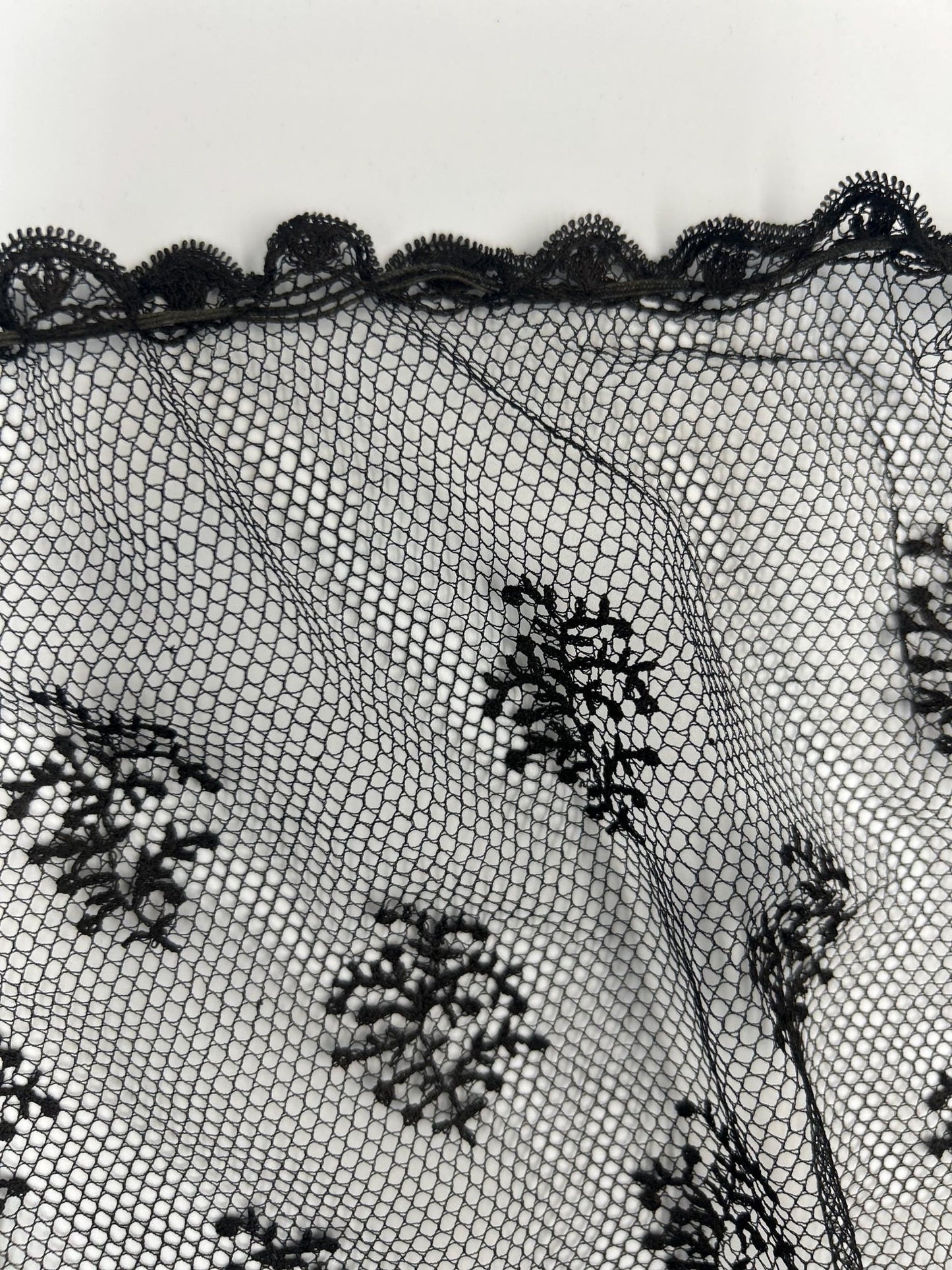 Antique black lace bonnet veil, lace panel close up of small floral detail and scalloped edge against light background