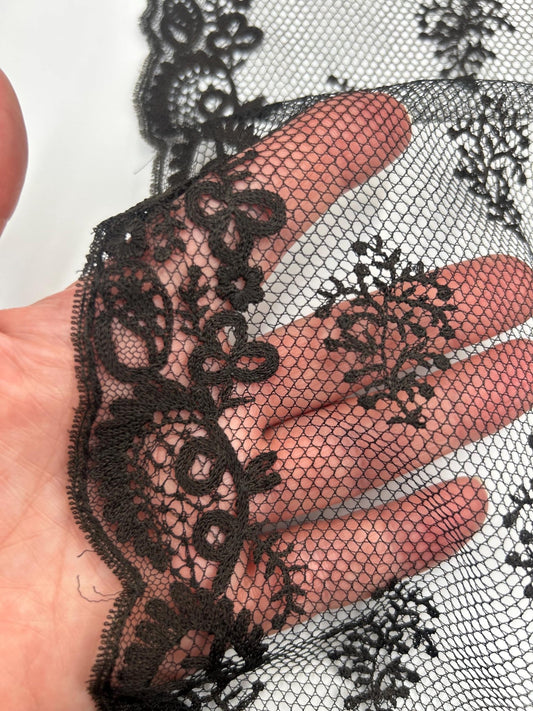 Antique black lace bonnet veil, apron, lace panel with scalloped edge close up with a hand behind against white background