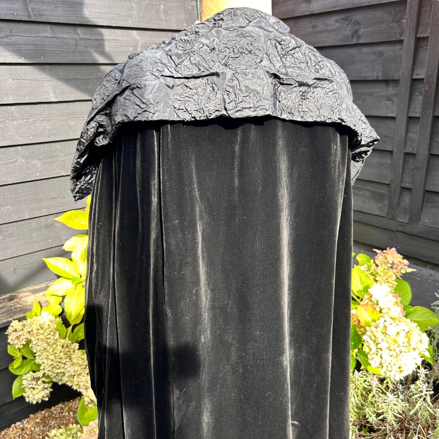 back view of Art Deco black velvet cocoon cape with feature collar on mannequin in garden background - Splendid Vintage World