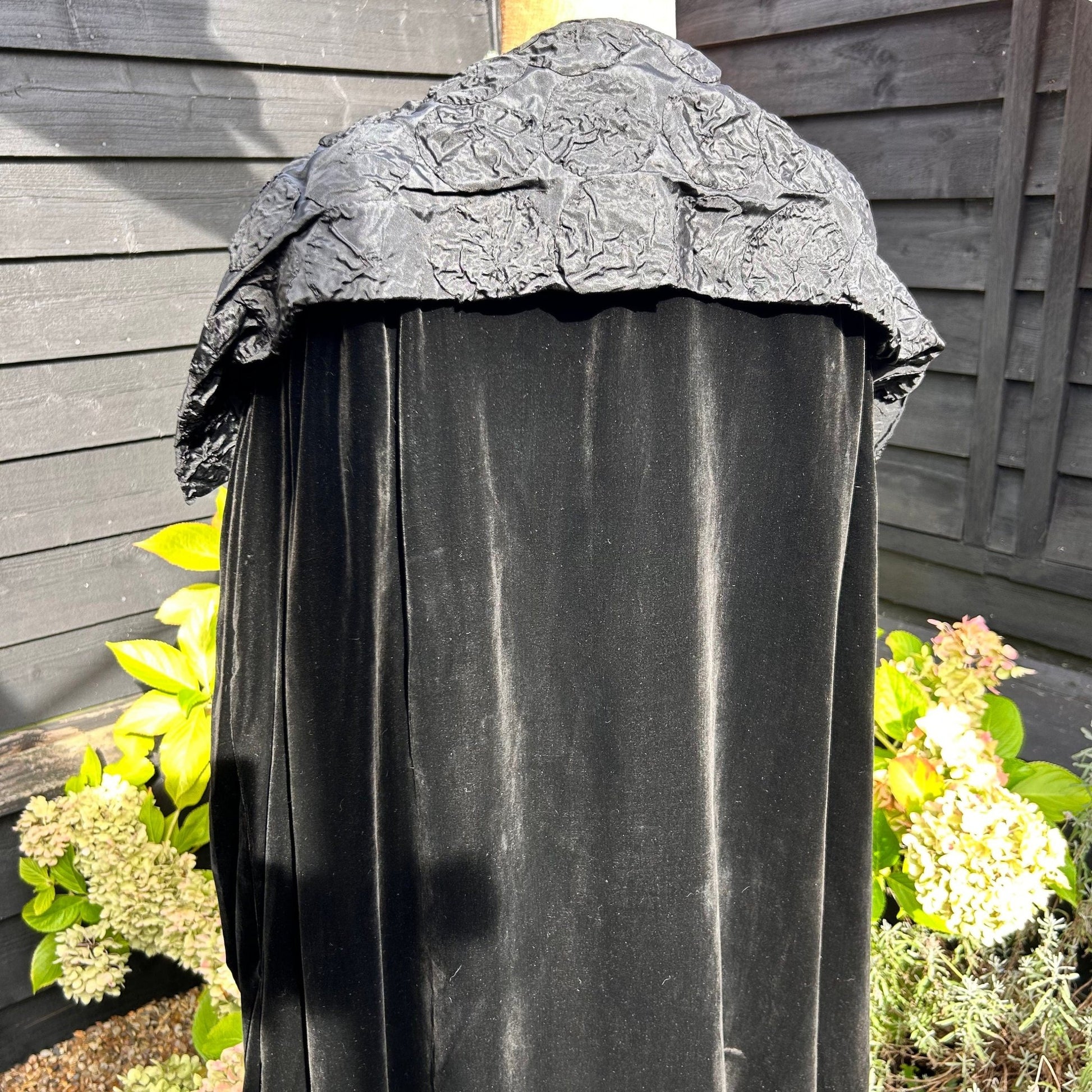 back view of Art Deco black velvet cocoon cape with feature collar on mannequin in garden background - Splendid Vintage World
