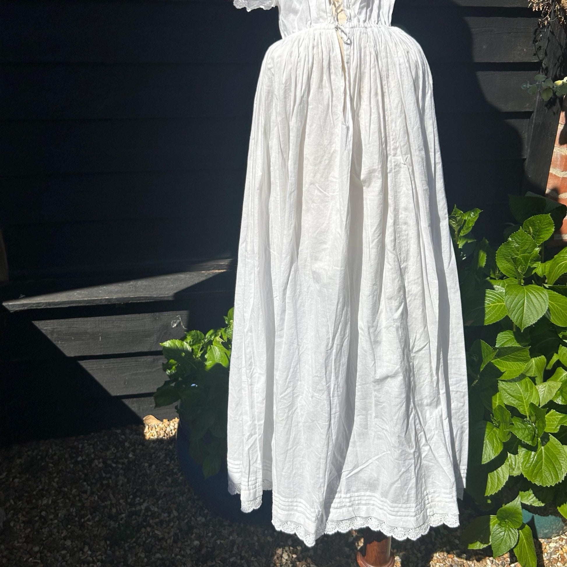 Antique white cotton Christening Gown skirt against greenery and black fence - Splendid Vintage World