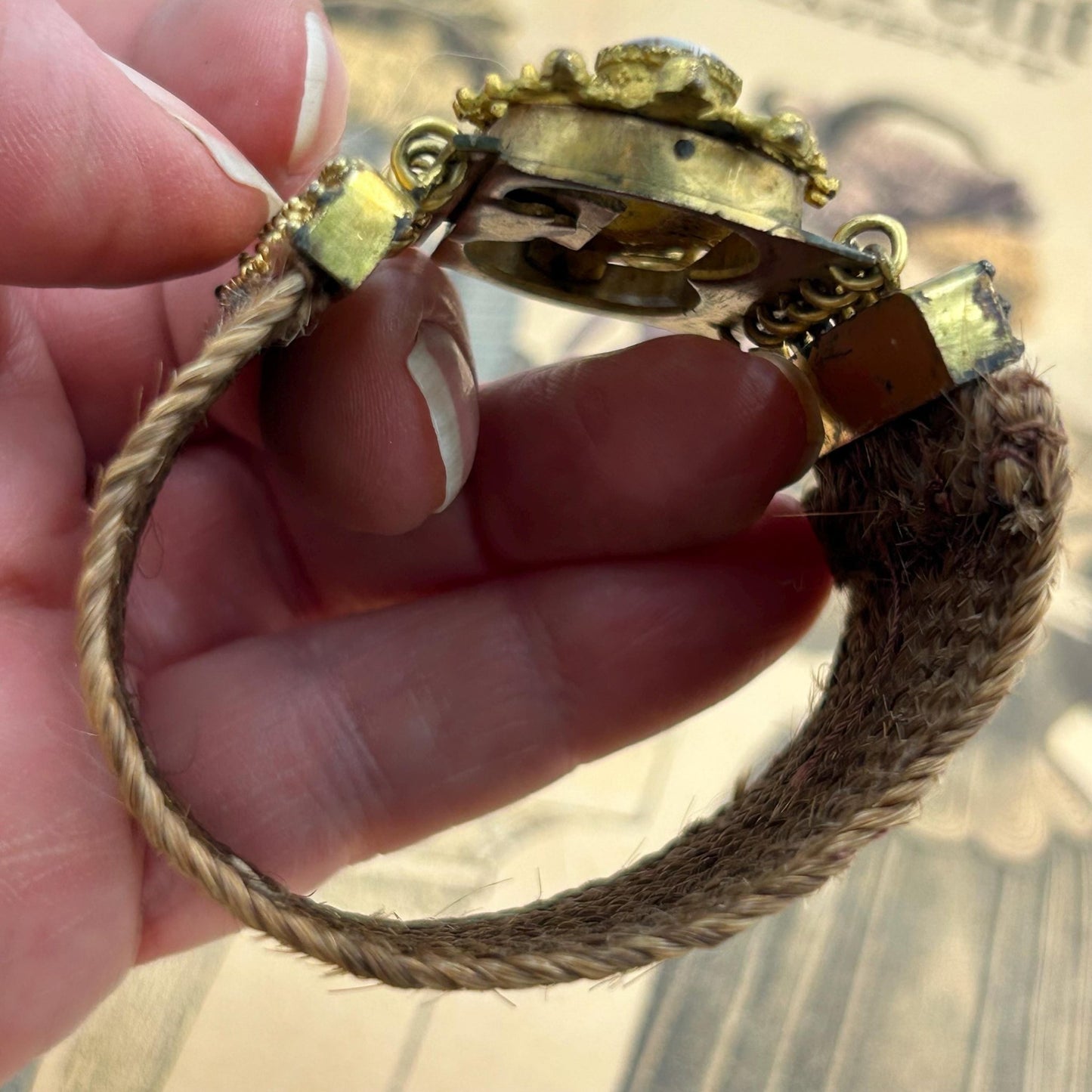 Antique Georgian Woven Hair Cuff Bracelet Gilt Metal held by hand above printed victorian magazine - Splendid Vintage World