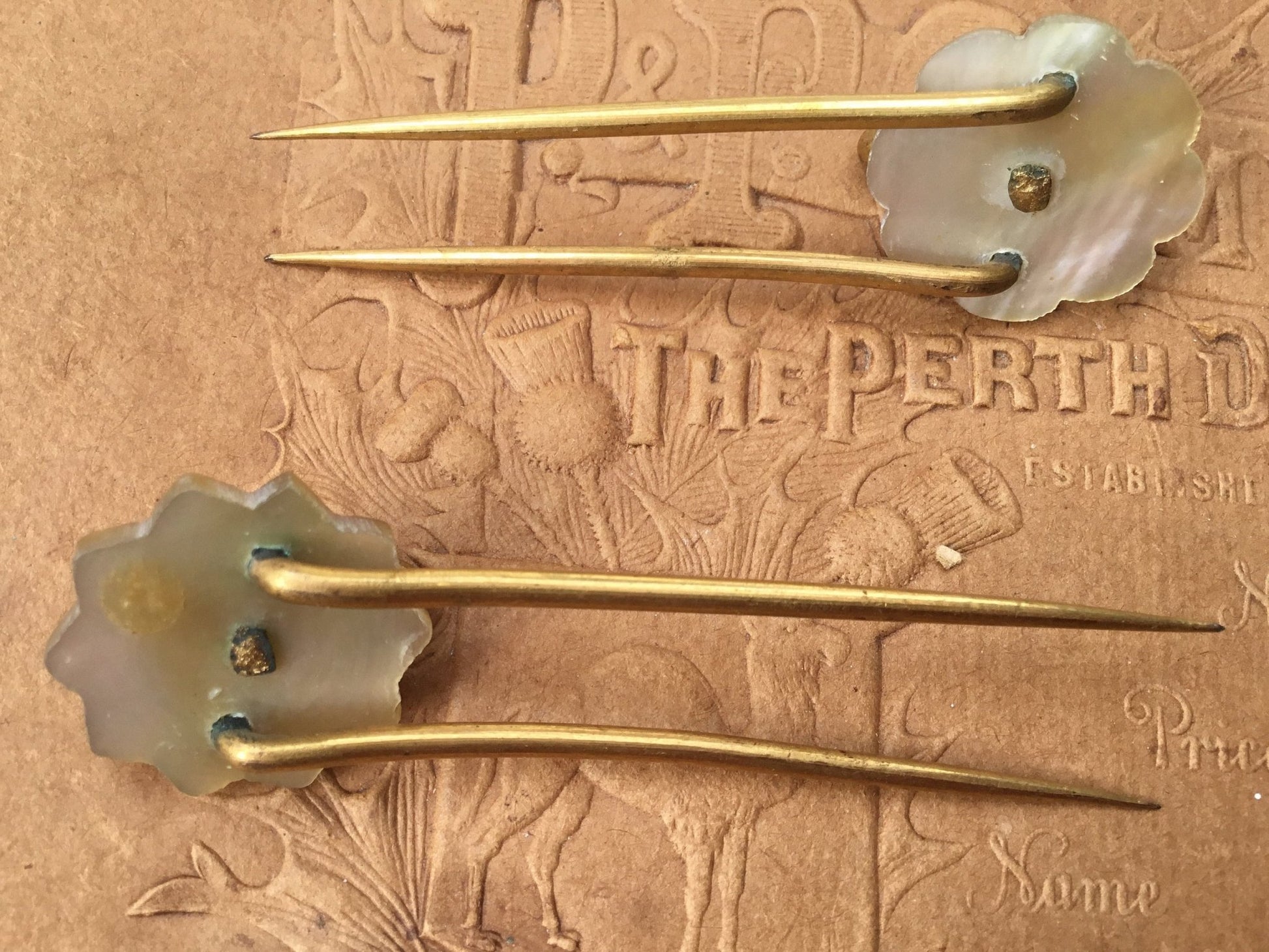 old coloured Hair pins with mother of pearl circular top on textured brown background - Splendid Vintage World