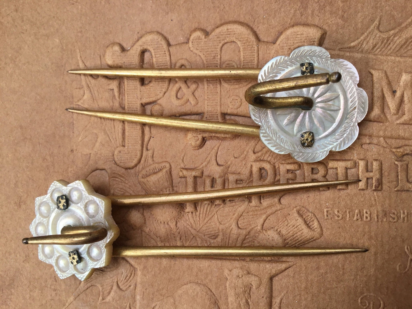 2 gold coloured Hair pins with mother of pearl circular top on textured brown background- Splendid Vintage World