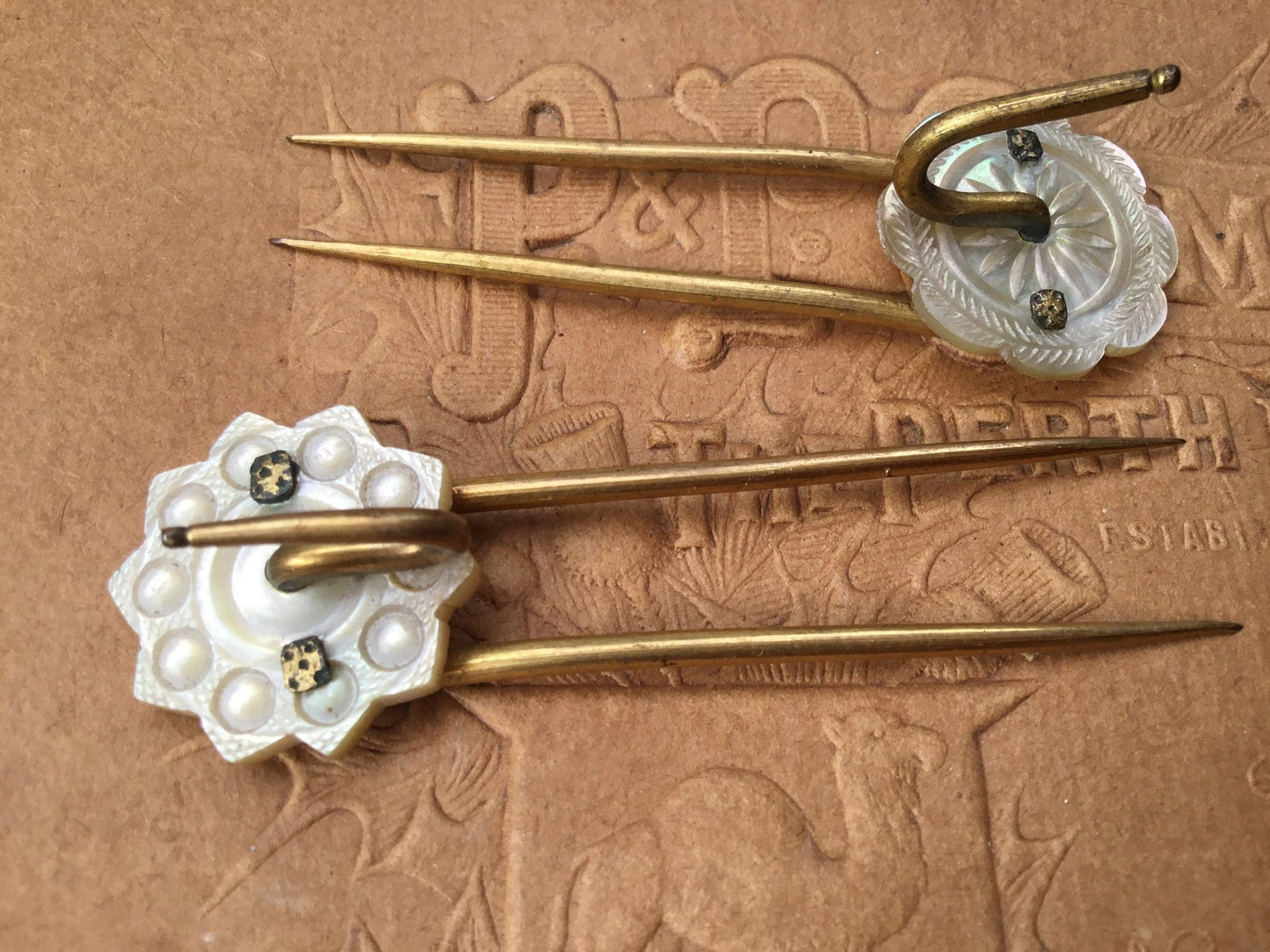 2 gold coloured Hair pins with mother of pearl circular top on textured brown background - Splendid Vintage World