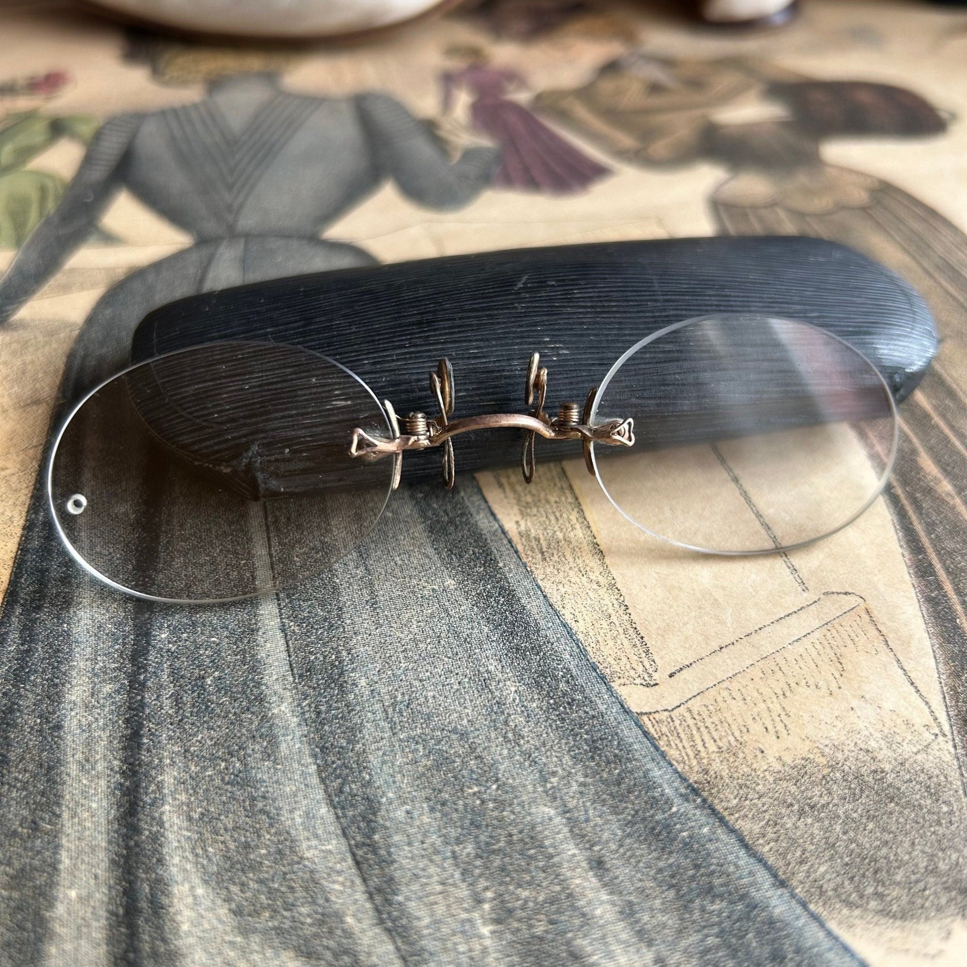 Antique Pince Nez Reading Spectacles against a glasses Case on printed clothing magazine - Splendid Vintage World