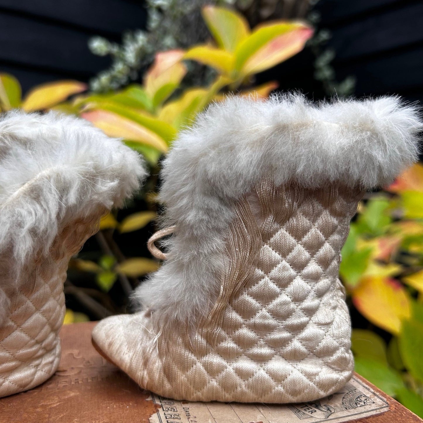 cream quilted textile with fur trim silk baby boots on wood surface with planting behind - Splendid Vintage World