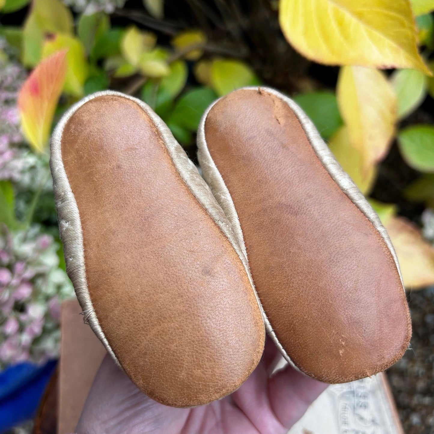 brown leather soles of baby boots held in hand against plants - Splendid Vintage World
