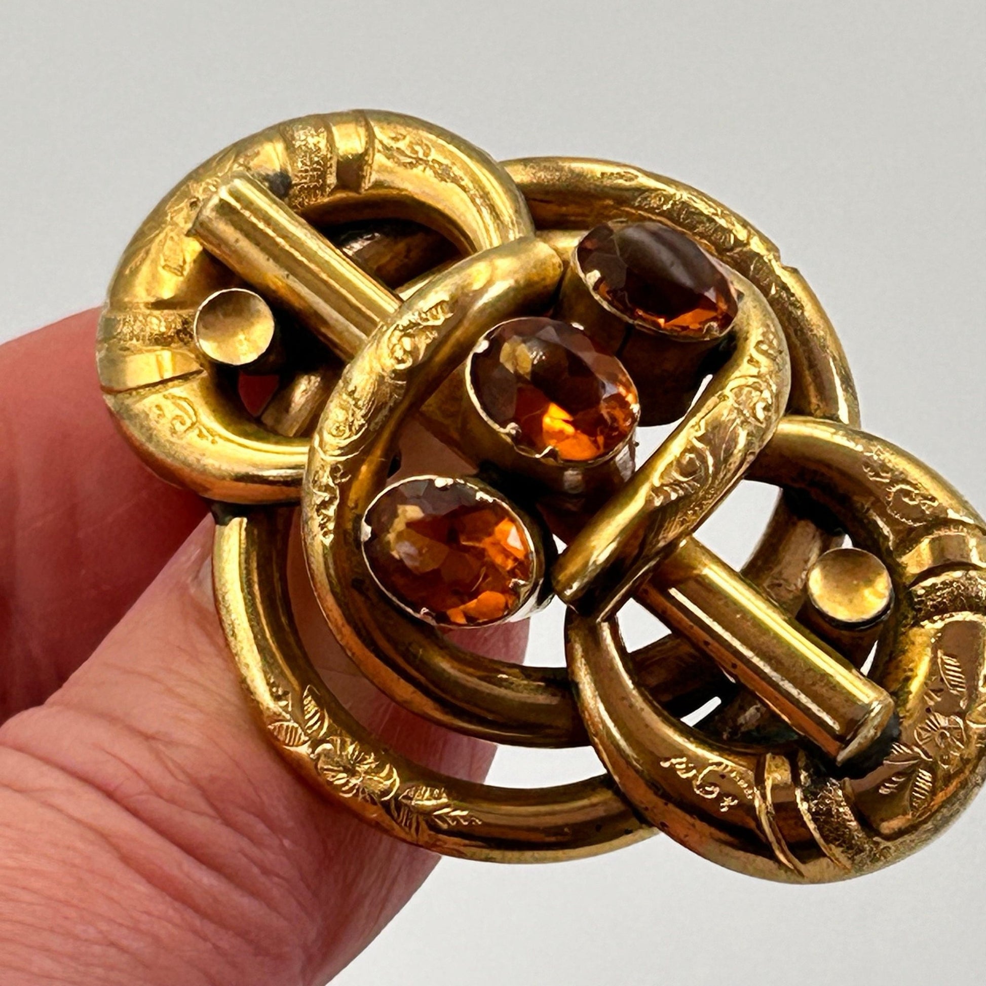 Antique 3 citrine stone & gold coloured lovers knot brooch held by hand on light backdrop - Splendid Vintage World