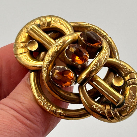 Antique 3 citrine stone & gold coloured lovers knot brooch held by hand on light backdrop - Splendid Vintage World