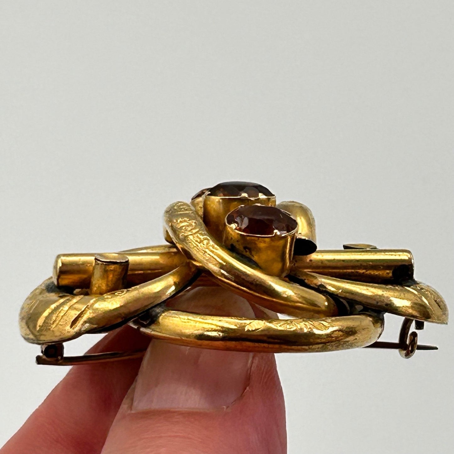 side view of Antique citrine paste & gold coloured lovers knot brooch held by hand on light backdrop - Splendid Vintage World