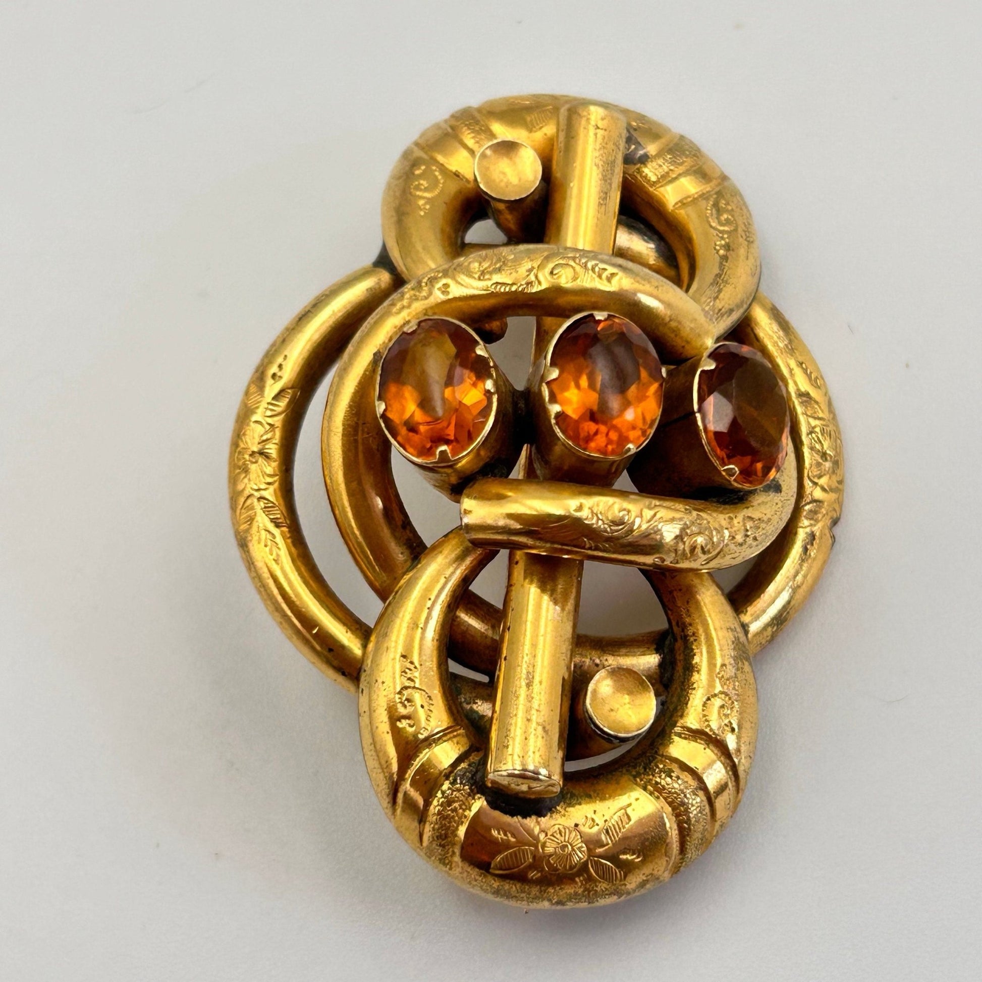 Victorian gold coloured brooch in lovers knot form, 3 oval citrine paste stones on light background - Splendid Vintage World