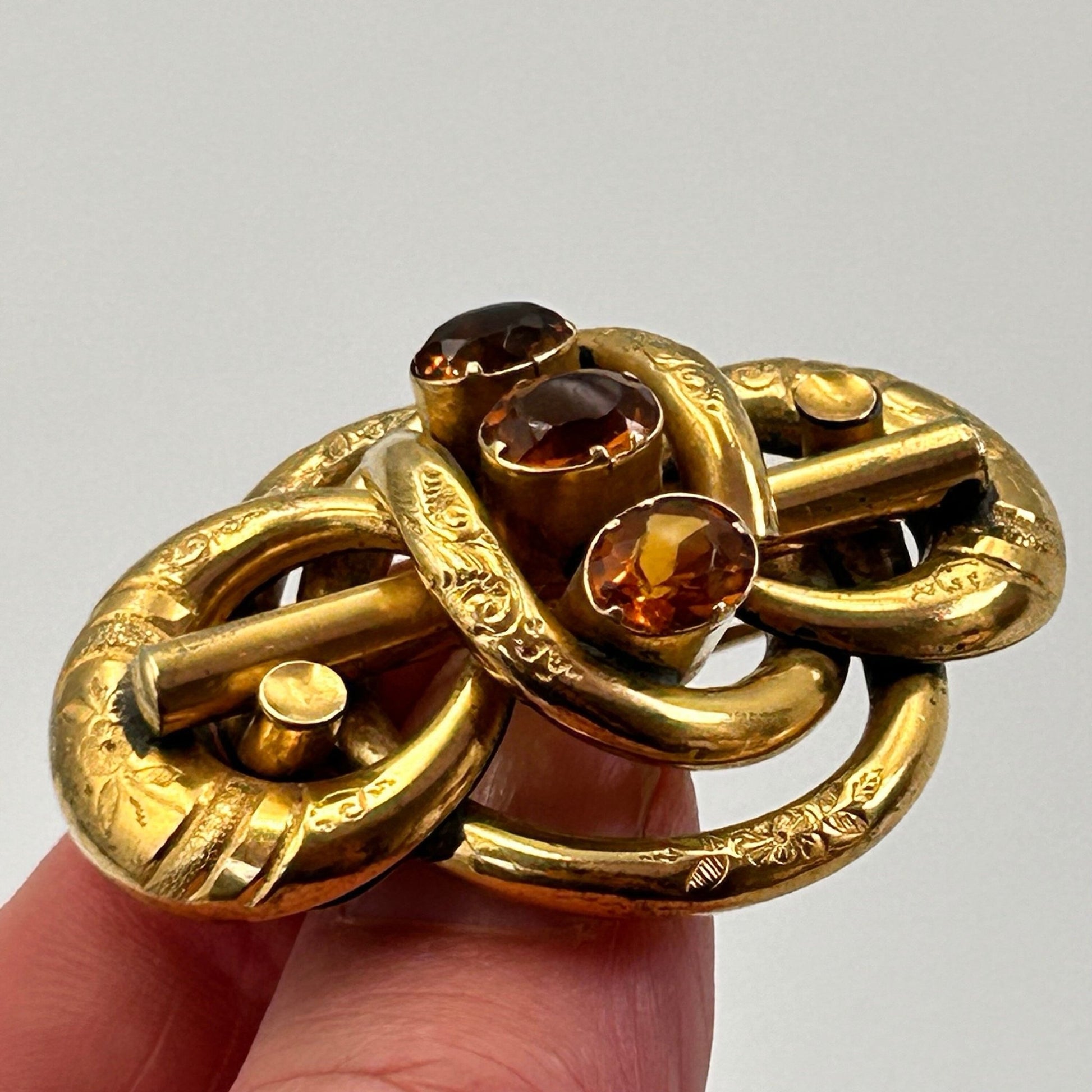antique gold coloured lovers knot brooch, 3 oval citrine paste stones held by hand on light backdrop - Splendid Vintage World