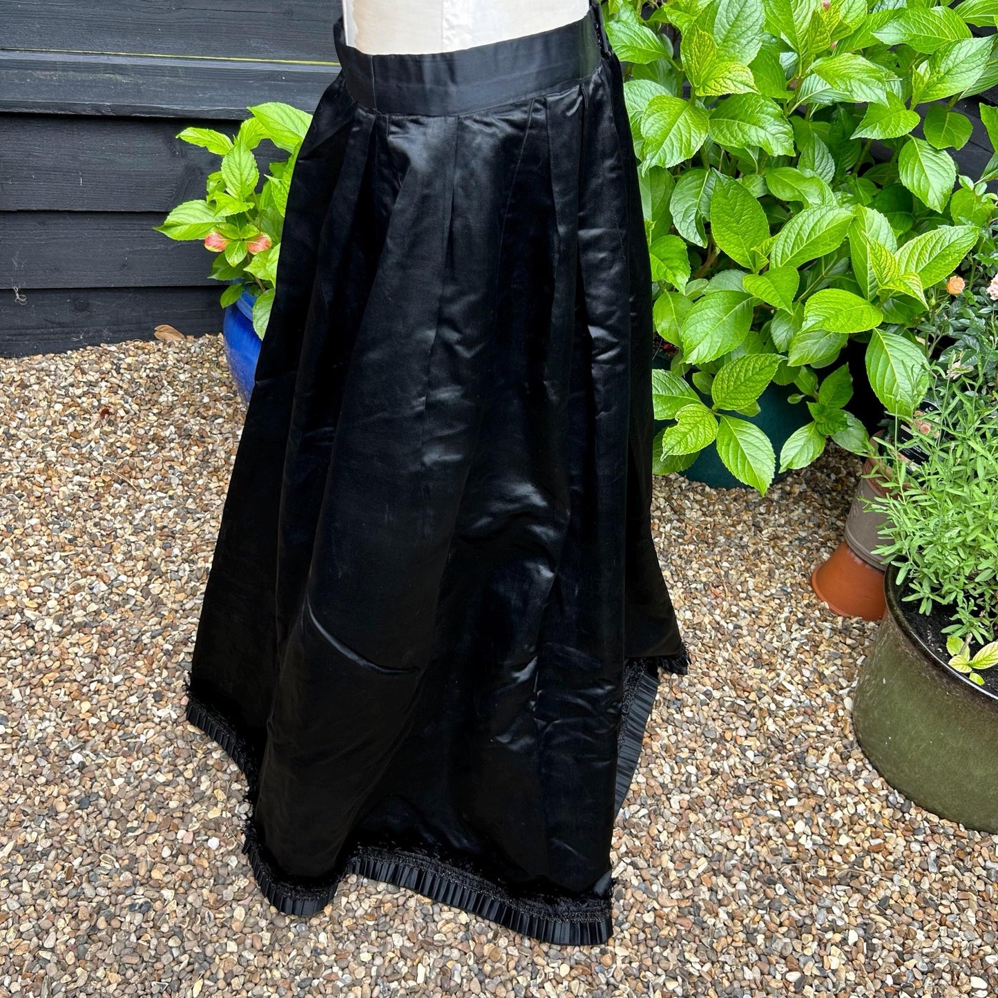 Antique black satin walking skirt Finely Pleated hem bead & silk tuft trim against shingle & green plant background