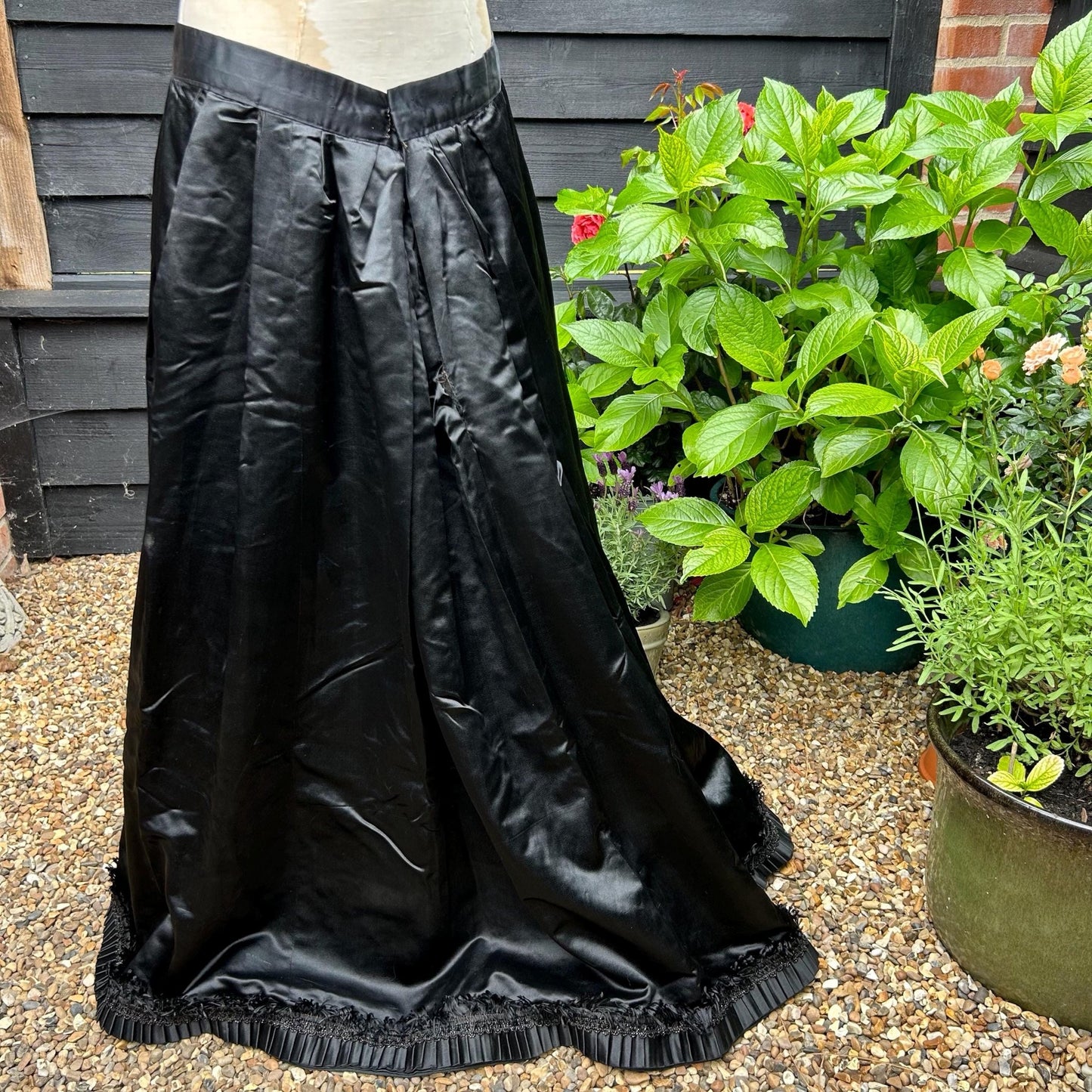 Antique black satin walking skirt slightly longer back hem finely pleated hem with bead & silk trim with green plants behind