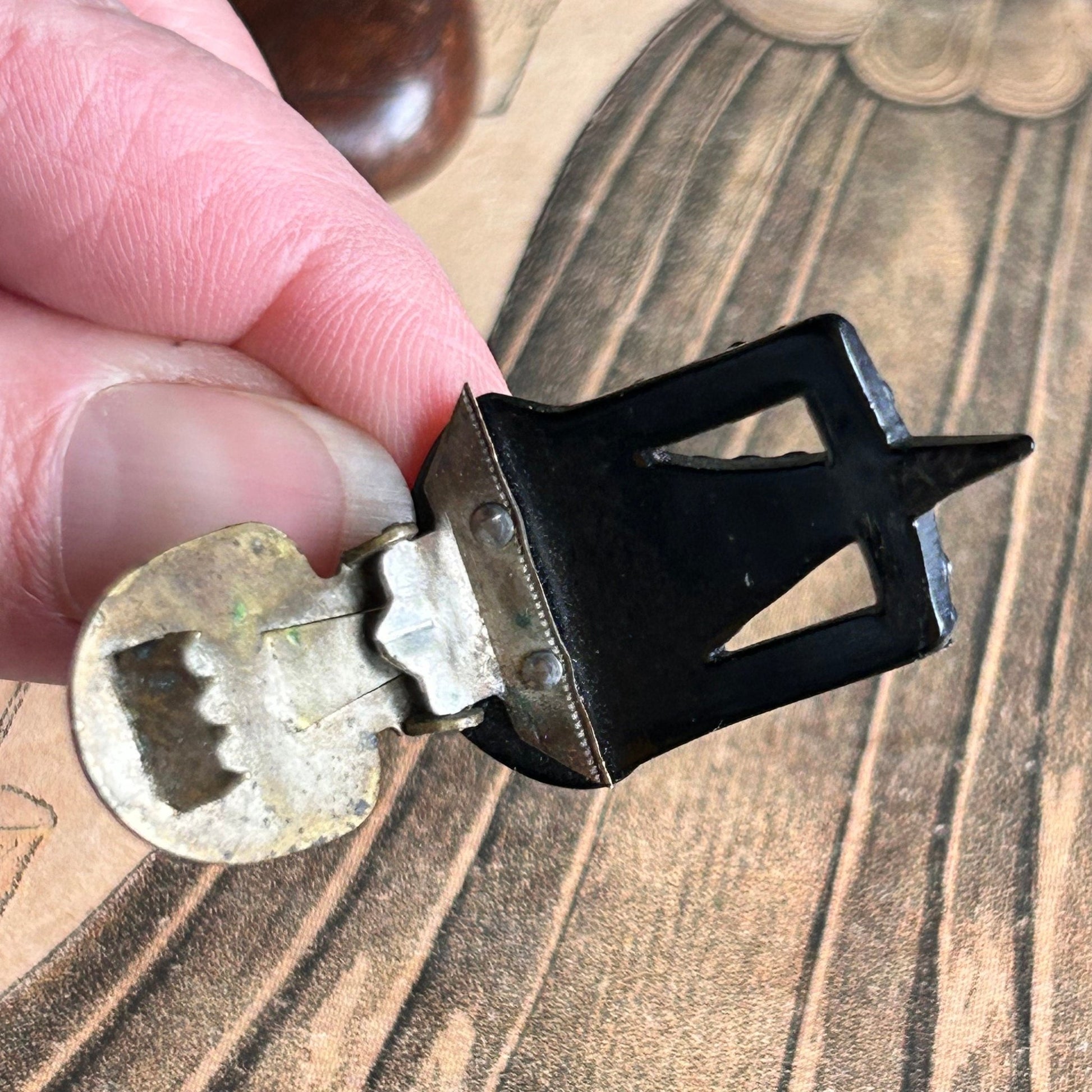 Art Deco 1930s dress clip being held showing the metal back clip above an old illustration - Splendid Vintage World