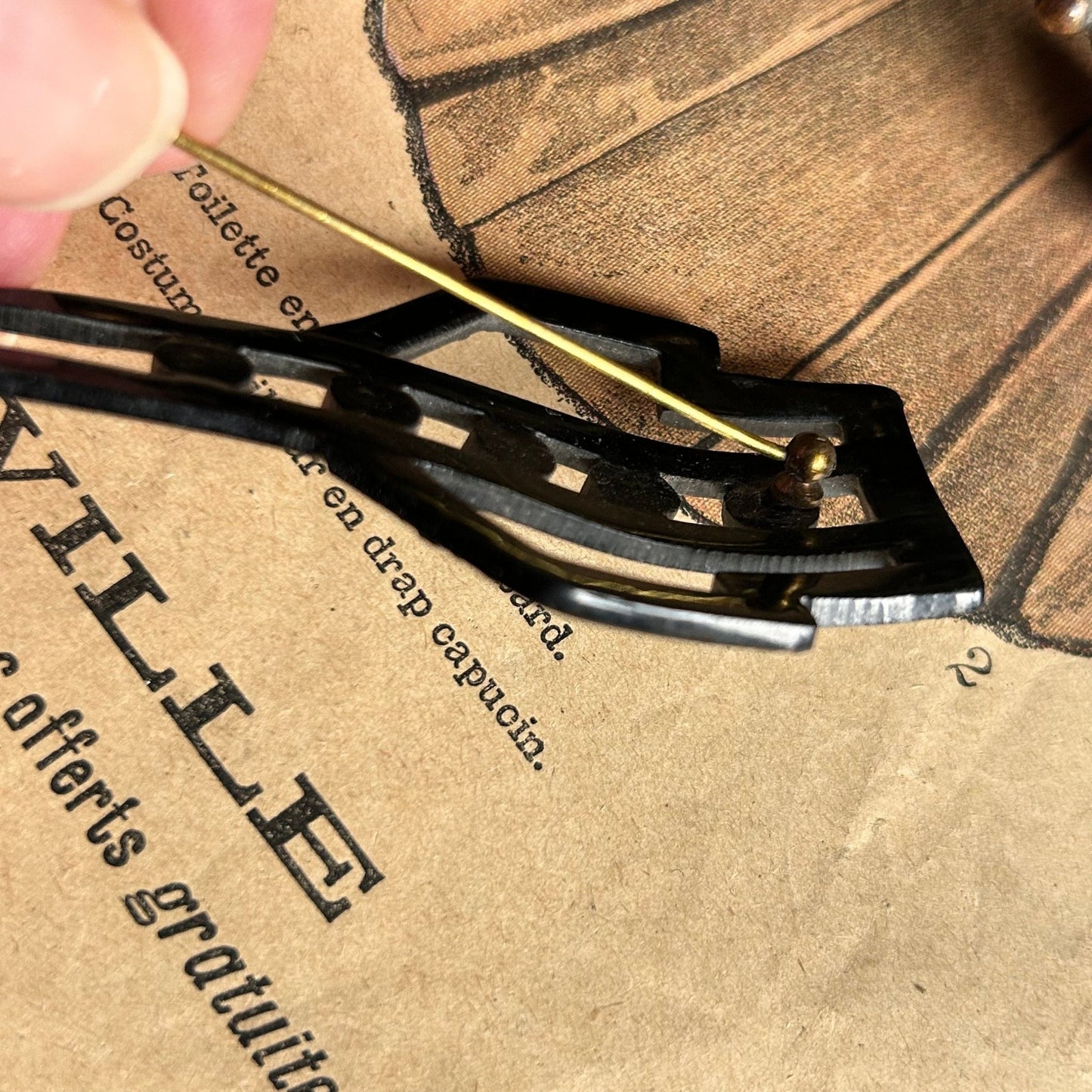 back view of brass pin of Art Deco black hat flash on illustrated magazine background - Splendid Vintage World