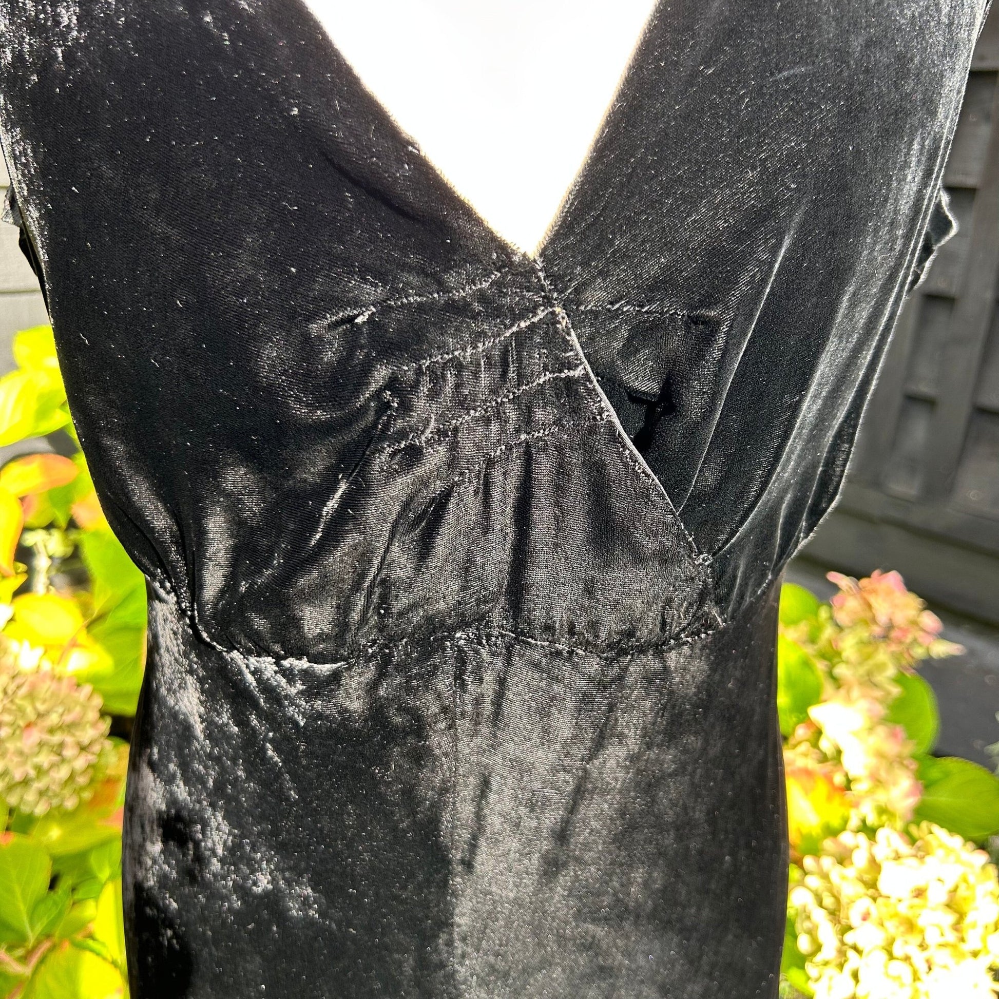 close up of v neck bodice of black velvet sleeveless dress against greenery - Splendid Vintage World