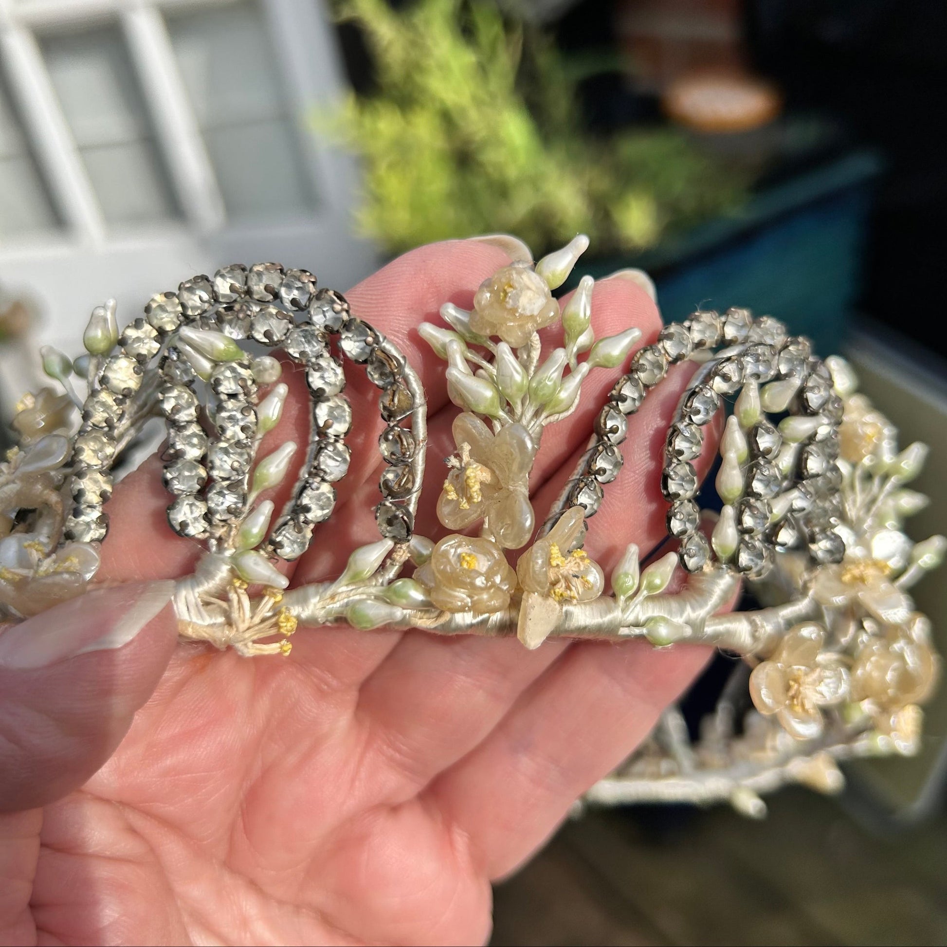 Vintage bridal crown tiara of diamanté, wax flowers & buds held in hand with blurred background - Splendid Vintage World