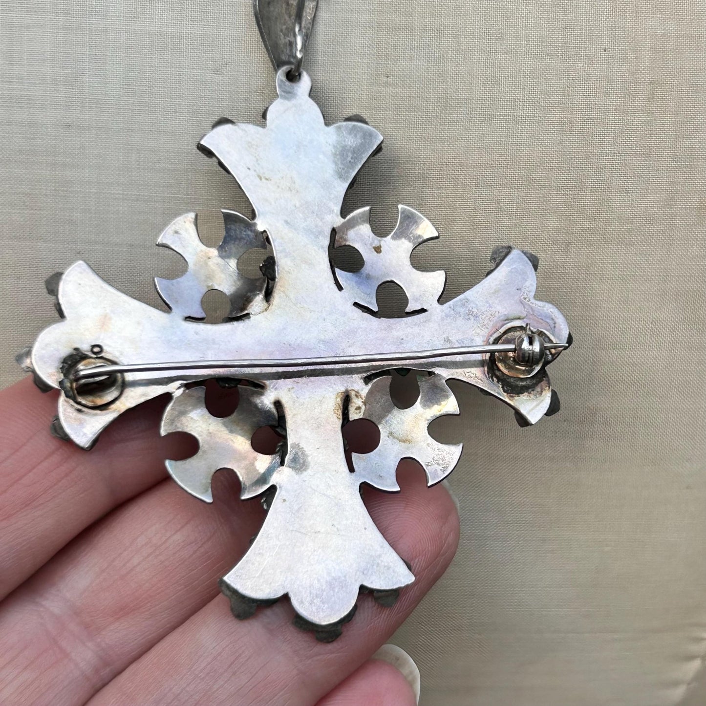 back of silver cross pendant with brooch fitting held by hand on beige backdrop - Splendid Vintage World