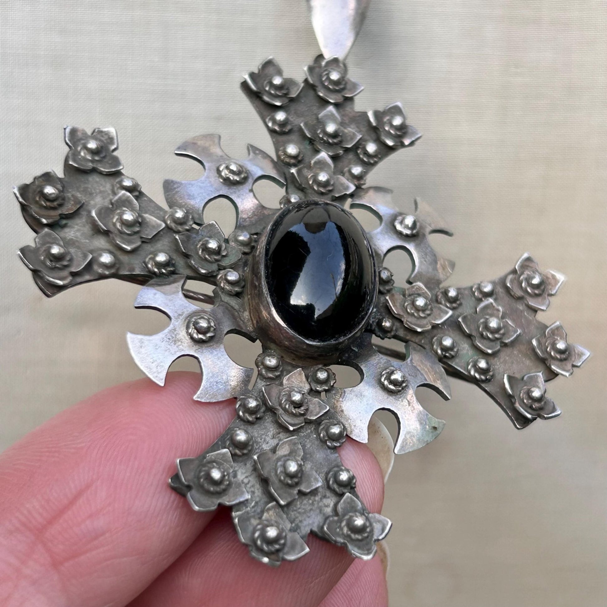 Vintage ornate silver cross pendant, Set with black cabochon held by hand on beige background - Splendid Vintage World
