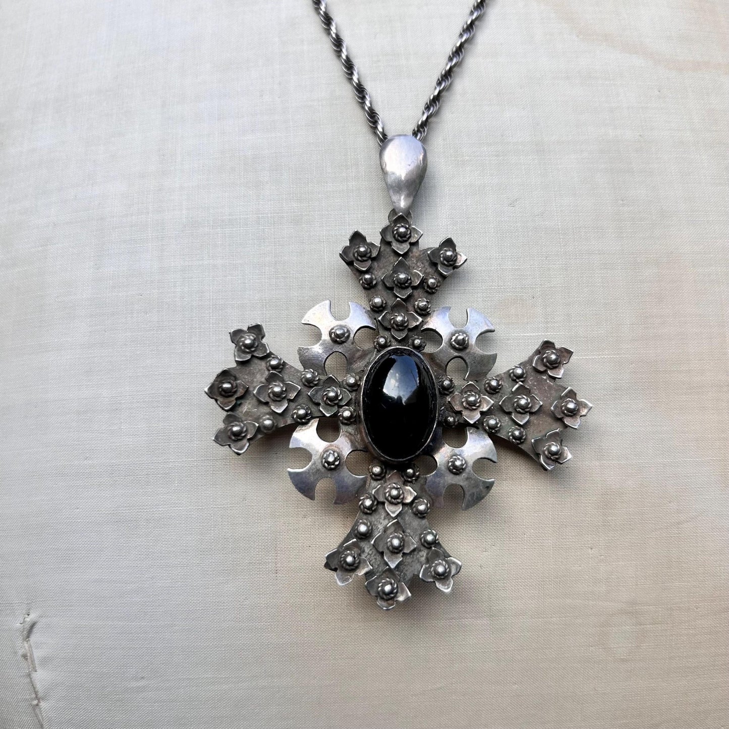 ornate silver cross pendant Set with oval black cabochon on silver rope chain on beige background - Splendid Vintage World
