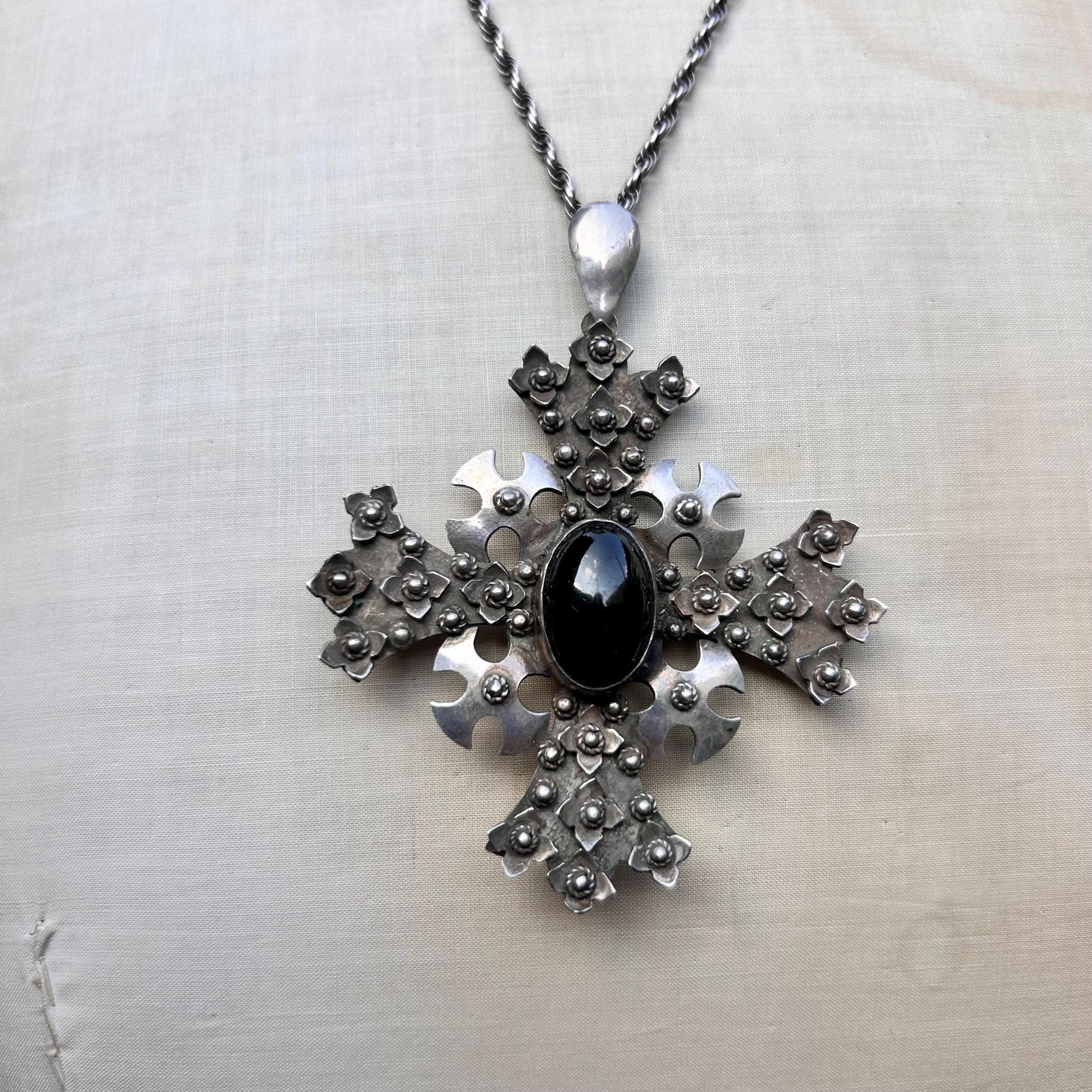 ornate silver cross pendant Set with oval black cabochon on silver rope chain on beige background - Splendid Vintage World