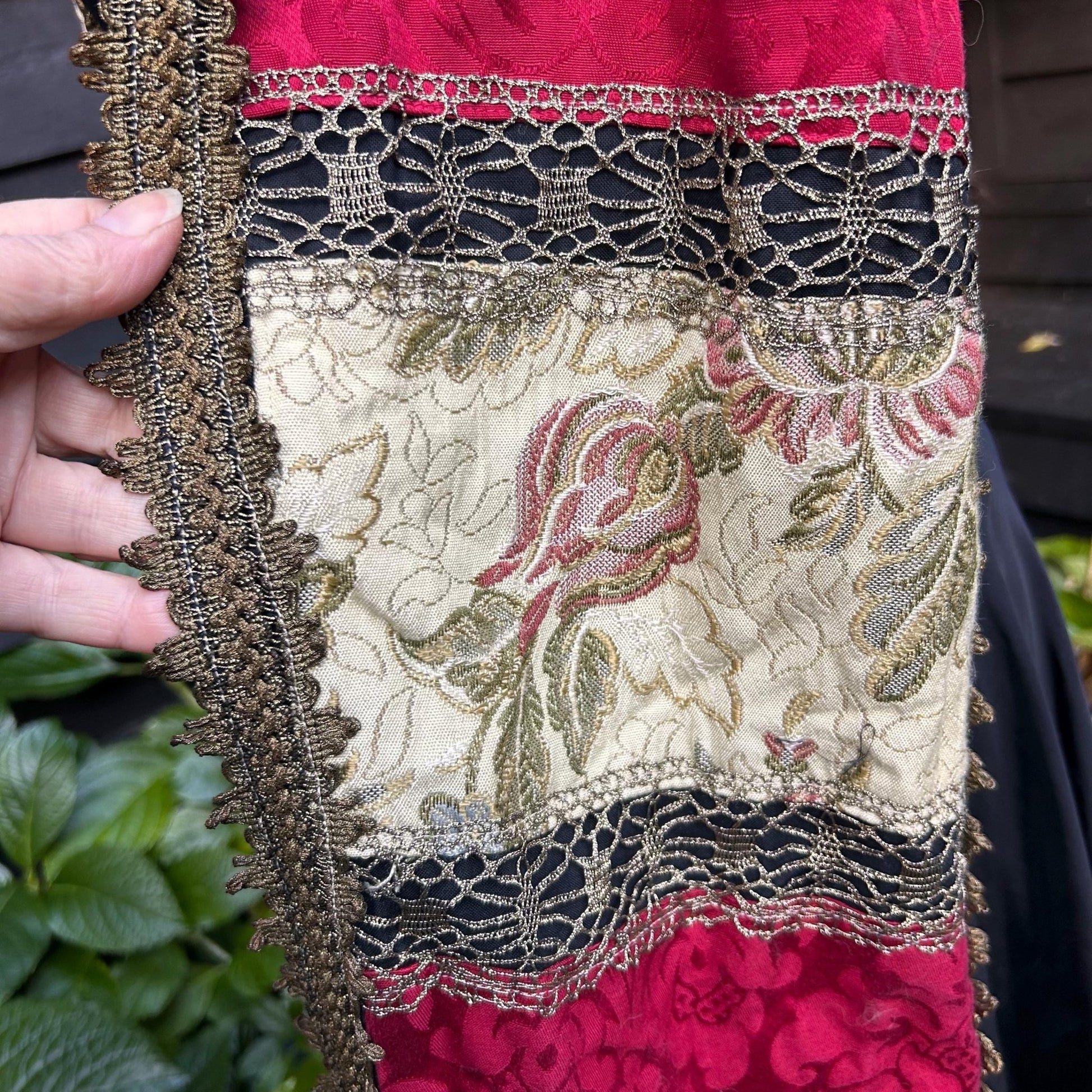cream patterned fabric with Gold Metallic Trim edge & red fabric strips held by hand greenery behind - Splendid Vintage World